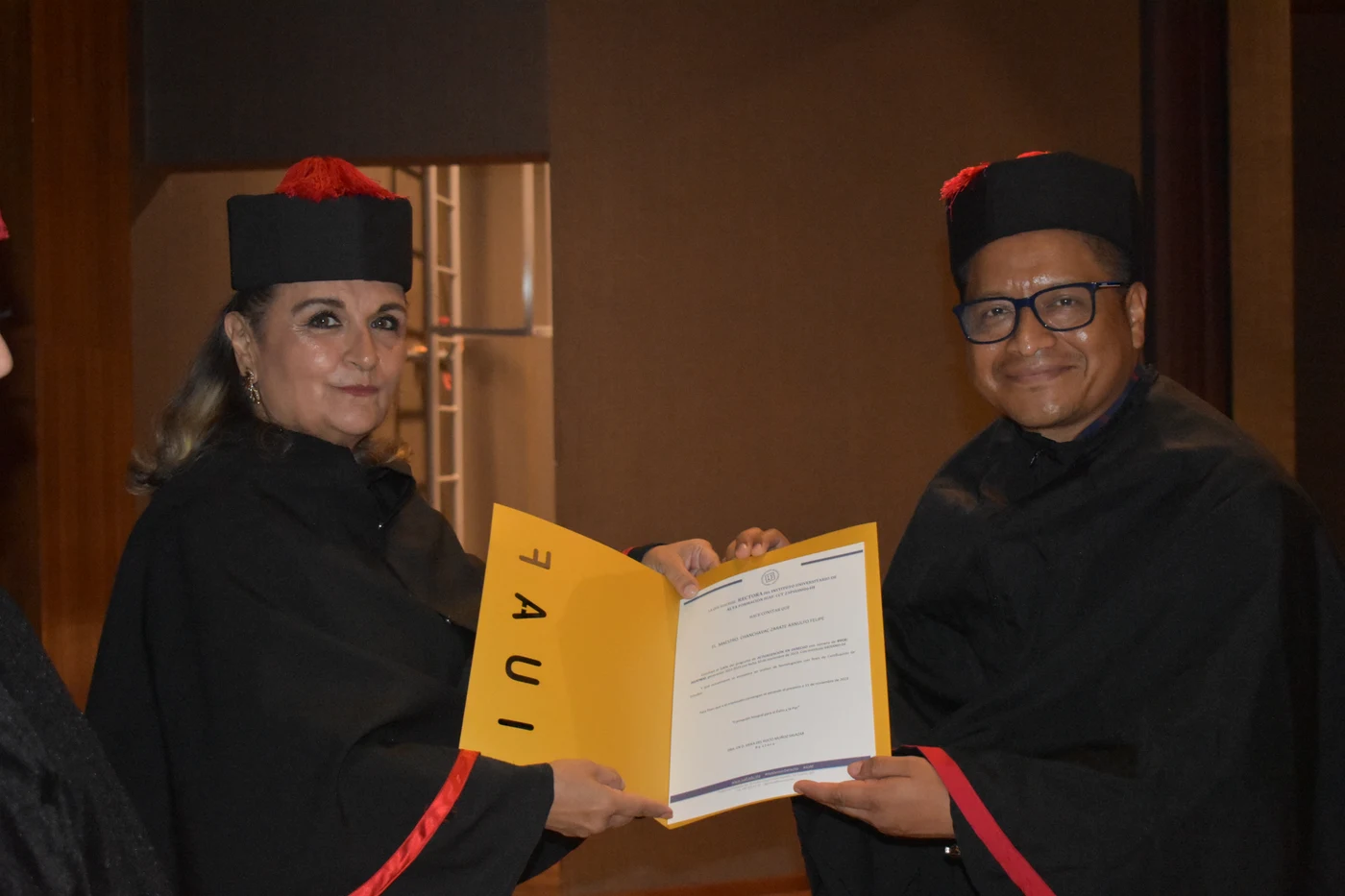 Dos personas con toga y birrete sostienen un diploma de IUAF durante una ceremonia